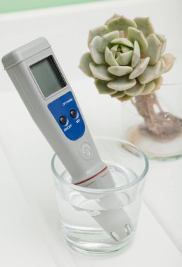 Bir bardak suda pH metre ve beyaz bir zeminde bitki kökü. İçme suyu özelliklerinin ölçümü. Suyun sertliği. İçme suyu kalite analizörü.
