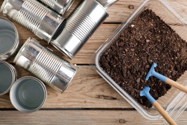 Evde yaratıcı geri dönüşüm, alüminyum kutular ve bahçedeki ahşap masa üzerinde toprak olan geri dönüştürülmüş plastik kaplar.
