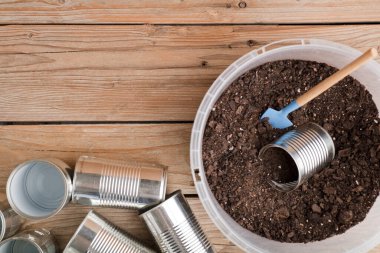 Evde yaratıcı geri dönüşüm, alüminyum kutular ve bahçedeki ahşap masa üzerinde toprak olan geri dönüştürülmüş plastik kaplar.