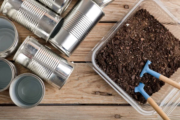 Evde yaratıcı geri dönüşüm, alüminyum kutular ve bahçedeki ahşap masa üzerinde toprak olan geri dönüştürülmüş plastik kaplar.