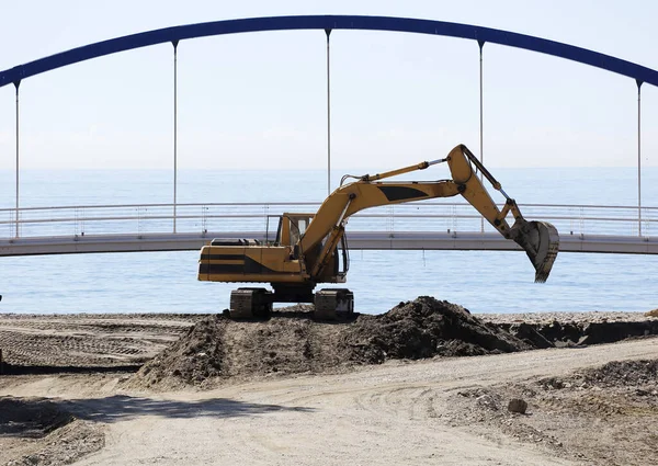 excavation and earthmoving machinery, bulldozer with bridge and sea in the background. Cleaning of the river mouth into the sea.