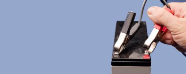 Beyaz adamın elinde pil cıvatası var. Pili pozitif ve negatif kutuplu, mavi arka planı var.