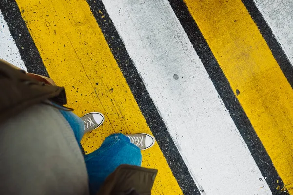 ジーンズの女性の足の上のスタイリッシュなカーキスニーカーは 黄色と白の交差点でストリートロードを横断します ストリートライフスタイル 選択的焦点 — ストック写真