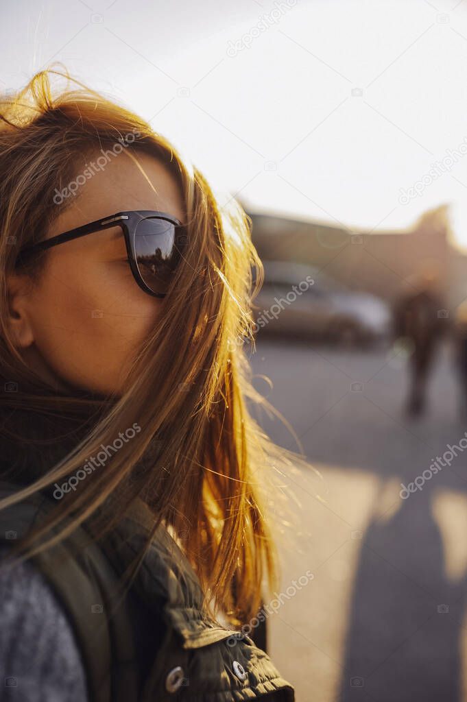 portrait of a young woman, her hair shines beautifully in the sun at sunset, develops and covers her face. a stylish image of a woman. vertical, selective focus