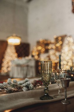 Bej ve ahşap renklerde şık bir Noel masası, altın çatal bıçaklı cam kaşık, mum, pamuk ve çelenkler, sahte bir arkaplan ve Noel arkaplanına karşı, seçici bir odak