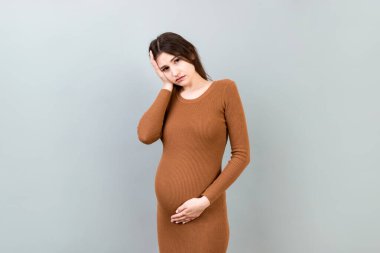 Güzel, genç, hamile bir kadın, renkli bir arka planda baş ağrısı çekiyor. Stresli hamile kadın ya da anne sorunları.