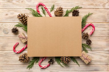 Noel kompozisyonu düzdü. Kare kağıt boş, çam ağacı dalları, renkli arka planda noel süslemeleri. Üst görünüm, metin için boşluk kopyala.