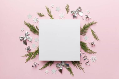 Noel kompozisyonu düzdü. Kare kağıt boş, çam ağacı dalları, renkli arka planda noel süslemeleri. Üst görünüm, metin için boşluk kopyala.