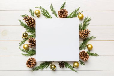 Noel kompozisyonu düzdü. Kare kağıt boş, çam ağacı dalları, renkli arka planda noel süslemeleri. Üst görünüm, metin için boşluk kopyala.