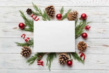 Noel kompozisyonu düzdü. Kare kağıt boş, çam ağacı dalları, renkli arka planda noel süslemeleri. Üst görünüm, metin için boşluk kopyala.
