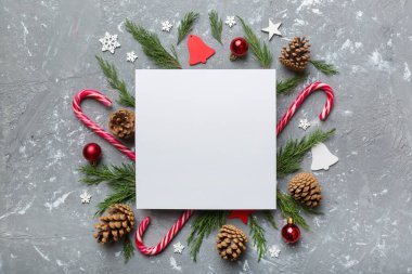 Noel kompozisyonu düzdü. Kare kağıt boş, çam ağacı dalları, renkli arka planda noel süslemeleri. Üst görünüm, metin için boşluk kopyala.