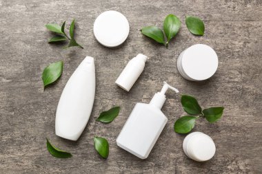 Çimento arka planında yeşil yaprakları olan organik kozmetik ürünler. Düz yatıyordu.