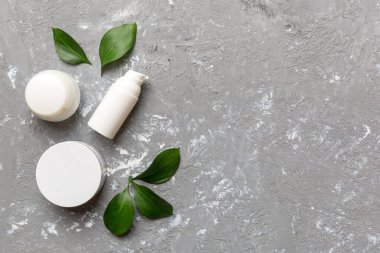 Çimento arka planında yeşil yaprakları olan organik kozmetik ürünler. Uzayı kopyala, düz yat.