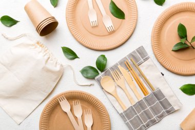 Açık beyaz masa arkaplanındaki boş, tek kullanımlık çevre dostu tabaklar, bardaklar, çatal bıçaklar. Üst Manzara. Biyo-çözünebilir el yapımı yemekler. Geri dönüşüm konsepti. Yakın plan..