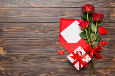 Zarflı sevgililer günü kompozisyonu, gül çiçeği ve kırmızı kalp masada. Üst manzara, düz yatış. Tatil kavramı.
