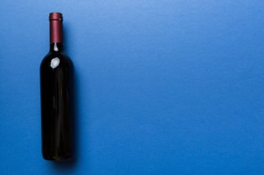 Renkli masada bir şişe kırmızı şarap. Düz konum, üst görünüm kopyalama alanı.