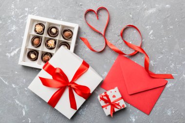 Sevgililer Günü için renkli arka planda hediye kutusu ve çikolatalı zarf. Kalp, hediye kutusuyla şekillendirilmiş çikolatalar fotokopi alanı ile üst görünüm.