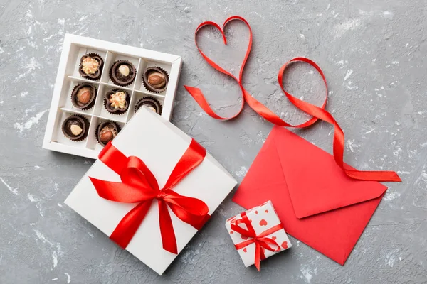 Sevgililer Günü için renkli arka planda hediye kutusu ve çikolatalı zarf. Kalp, hediye kutusuyla şekillendirilmiş çikolatalar fotokopi alanı ile üst görünüm.