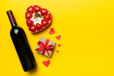 Sevgililer Günü için renkli arka planda bir şişe kırmızı şarap hediye ve çikolatalı. Kalp, hediye kutusuyla şekillendirilmiş çikolatalar fotokopi alanı ile üst görünüm.