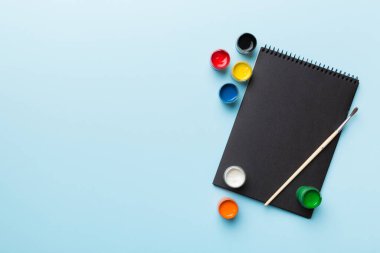 Albüm sayfaları, boyalar, kalemler, renkli arka planda fırçalar. Boşluğu olan üst görünüm. Yaratıcılık için işyeri. ev öğretmenliği kavramı çizimi.