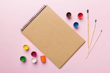 Albüm sayfaları, boyalar, kalemler, renkli arka planda fırçalar. Boşluğu olan üst görünüm. Yaratıcılık için işyeri. ev öğretmenliği kavramı çizimi.