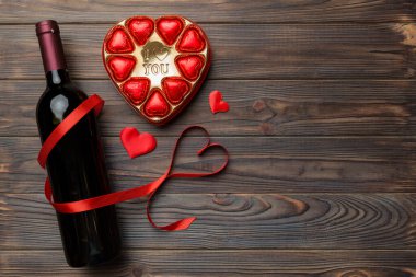 Sevgililer Günü için renkli arka planda bir şişe kırmızı şarap hediye ve çikolatalı. Kalp, hediye kutusuyla şekillendirilmiş çikolatalar fotokopi alanı ile üst görünüm.