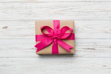 El işi kağıdına sarılı, masa arkasında renkli bir fiyonk olan tatil hediyesi kutusu. Üst görünüm, düz görünüm, kopyalama alanı.