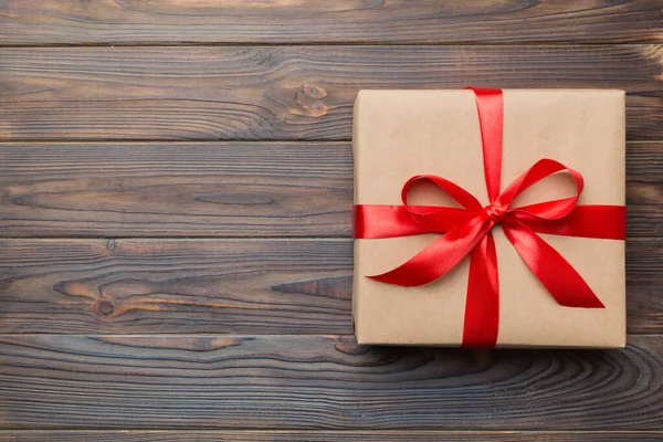 El işi kağıdına sarılı, masa arkasında renkli bir fiyonk olan tatil hediyesi kutusu. Üst görünüm, düz görünüm, kopyalama alanı.