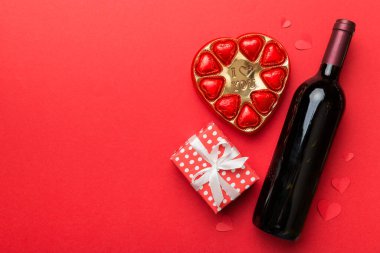 Sevgililer Günü için renkli arka planda bir şişe kırmızı şarap hediye ve çikolatalı. Kalp, hediye kutusuyla şekillendirilmiş çikolatalar fotokopi alanı ile üst görünüm.