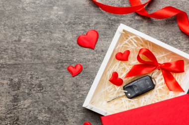 Siyah araba anahtarı, renkli arka planda kırmızı kalp ve kurdele olan hediye kutusunda. Sevgililer Günü Kompozisyonu Üst Görünüm.