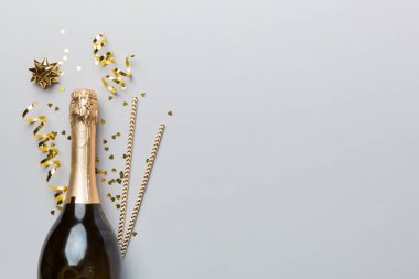 Gözlüklü bir şişe şampanya ve renkli arka planda renkli konfeti. Üst görünüm yatıyordu.