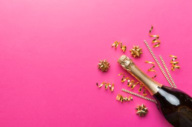 Gözlüklü bir şişe şampanya ve renkli arka planda renkli konfeti. Üst görünüm yatıyordu.