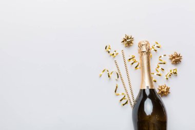 Gözlüklü bir şişe şampanya ve renkli arka planda renkli konfeti. Üst görünüm yatıyordu.