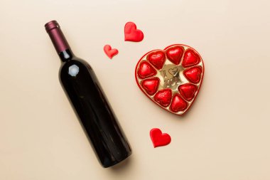 Sevgililer Günü için renkli arka planda bir şişe kırmızı şarap hediye ve çikolatalı. Kalp, hediye kutusuyla şekillendirilmiş çikolatalar fotokopi alanı ile üst görünüm.