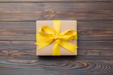 El işi kağıdına sarılı, masa arkasında renkli bir fiyonk olan tatil hediyesi kutusu. Üst görünüm, düz görünüm, kopyalama alanı.