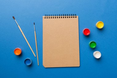 Albüm sayfaları, boyalar, kalemler, renkli arka planda fırçalar. Boşluğu olan üst görünüm. Yaratıcılık için işyeri. ev öğretmenliği kavramı çizimi.