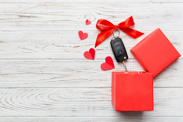 Siyah araba anahtarı, renkli arka planda kırmızı kalp ve kurdele olan hediye kutusunda. Sevgililer Günü Kompozisyonu Üst Görünüm.