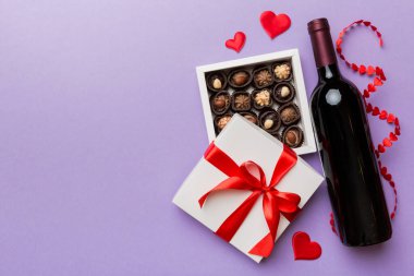 Sevgililer Günü için renkli arka planda bir şişe kırmızı şarap hediye ve çikolatalı. Kalp, hediye kutusuyla şekillendirilmiş çikolatalar fotokopi alanı ile üst görünüm.