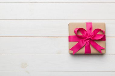 El işi kağıdına sarılı, masa arkasında renkli bir fiyonk olan tatil hediyesi kutusu. Üst görünüm, düz görünüm, kopyalama alanı.