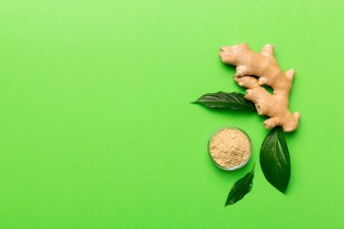 Renkli arka planda yeşil yapraklı kabın içinde zencefil tozu var. Üst görünüm düzlüğü.