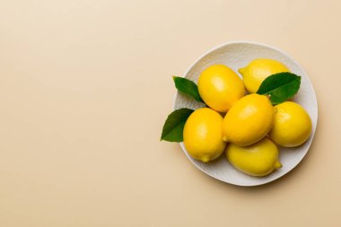 Taze kesilmiş limon ve tüm limonları renkli arka planda yuvarlak tabakta. Yemek ve içecek malzemeleri hazırlanıyor. Sağlıklı beslenme teması üst görünüm kopyalama alanı.