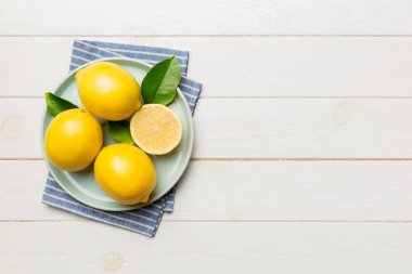 Taze kesilmiş limon ve tüm limonları renkli arka planda yuvarlak tabakta. Yemek ve içecek malzemeleri hazırlanıyor. Sağlıklı beslenme teması üst görünüm kopyalama alanı.