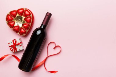 Sevgililer Günü için renkli arka planda bir şişe kırmızı şarap hediye ve çikolatalı. Kalp, hediye kutusuyla şekillendirilmiş çikolatalar fotokopi alanı ile üst görünüm.