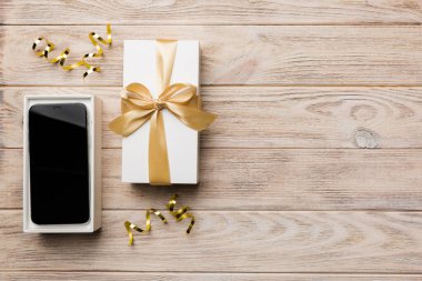 Altın kurdeleli hediye kutusu ve arka planda akıllı telefon, üst manzara. Boş kutu paketleme modeli, tasarımınız için şablon - markalaşma modeli.