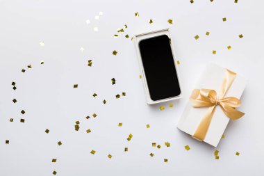 Altın kurdeleli hediye kutusu ve arka planda akıllı telefon, üst manzara. Boş kutu paketleme modeli, tasarımınız için şablon - markalaşma modeli.