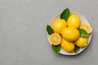 Taze kesilmiş limon ve tüm limonları renkli arka planda yuvarlak tabakta. Yemek ve içecek malzemeleri hazırlanıyor. Sağlıklı beslenme teması üst görünüm kopyalama alanı.