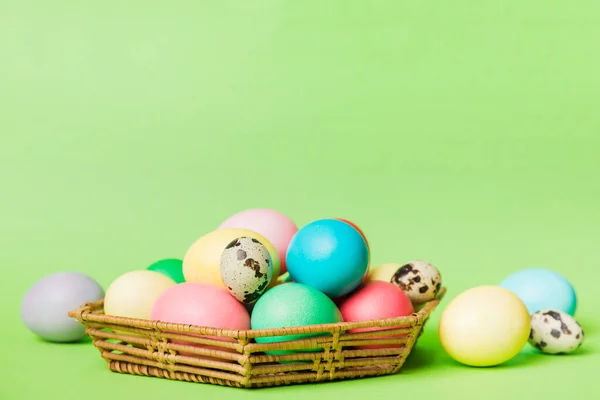 Multi colors Easter eggs in the woven basket on colored background . Pastel color Easter eggs. holiday concept with copy space.