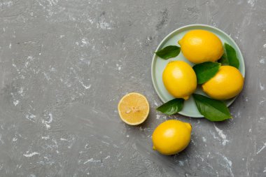 Taze kesilmiş limon ve tüm limonları renkli arka planda yuvarlak tabakta. Yemek ve içecek malzemeleri hazırlanıyor. Sağlıklı beslenme teması üst görünüm kopyalama alanı.