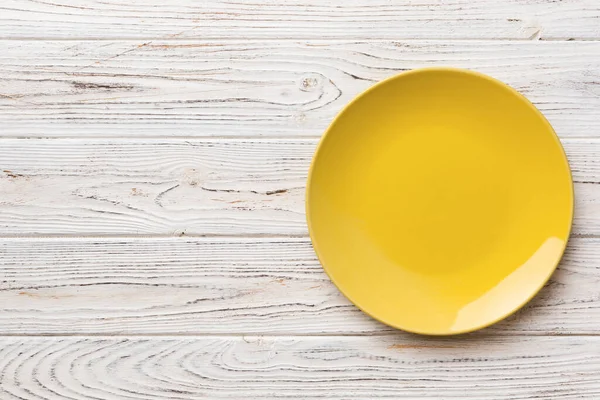 Ahşap arka planda boş sarı tabağın üst görüntüsü. Tasarımın için boş boşluk.