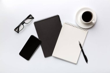 Modern ofis masası, defter, akıllı telefon ve kahve ile birlikte diğer malzemeler. Tasarım için boş defter sayfası. Üst manzara, düz uzanma.